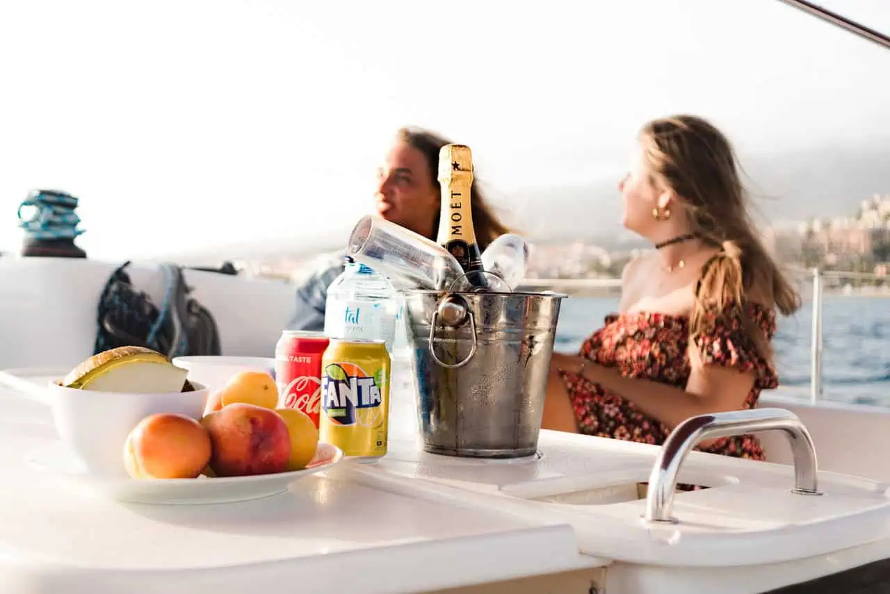 : A woman enjoys a chilled drink on the Atlantic Star, with fresh fruits and beverages laid out, adding to the relaxed ambiance of the sea trip.